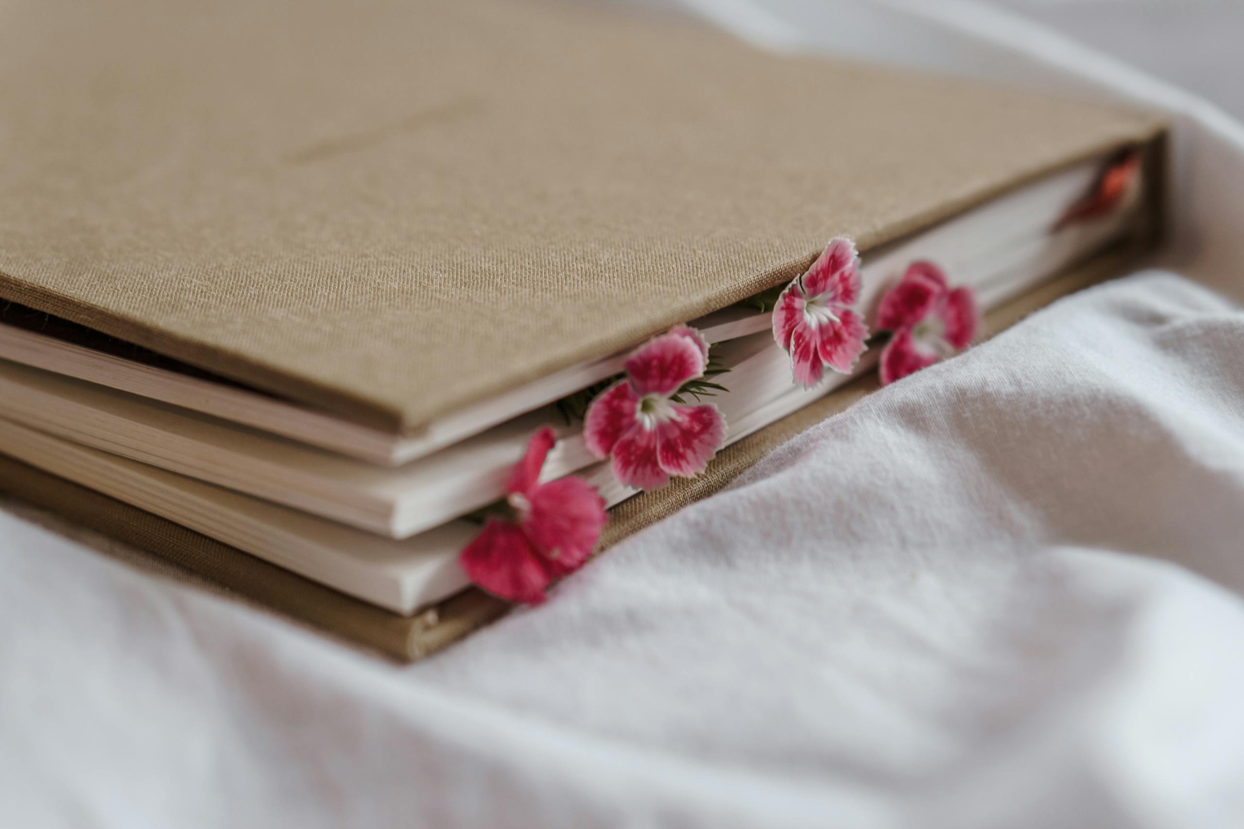 A beautiful beige journal adorned with pink floral bookmarks resting on soft white bedding.