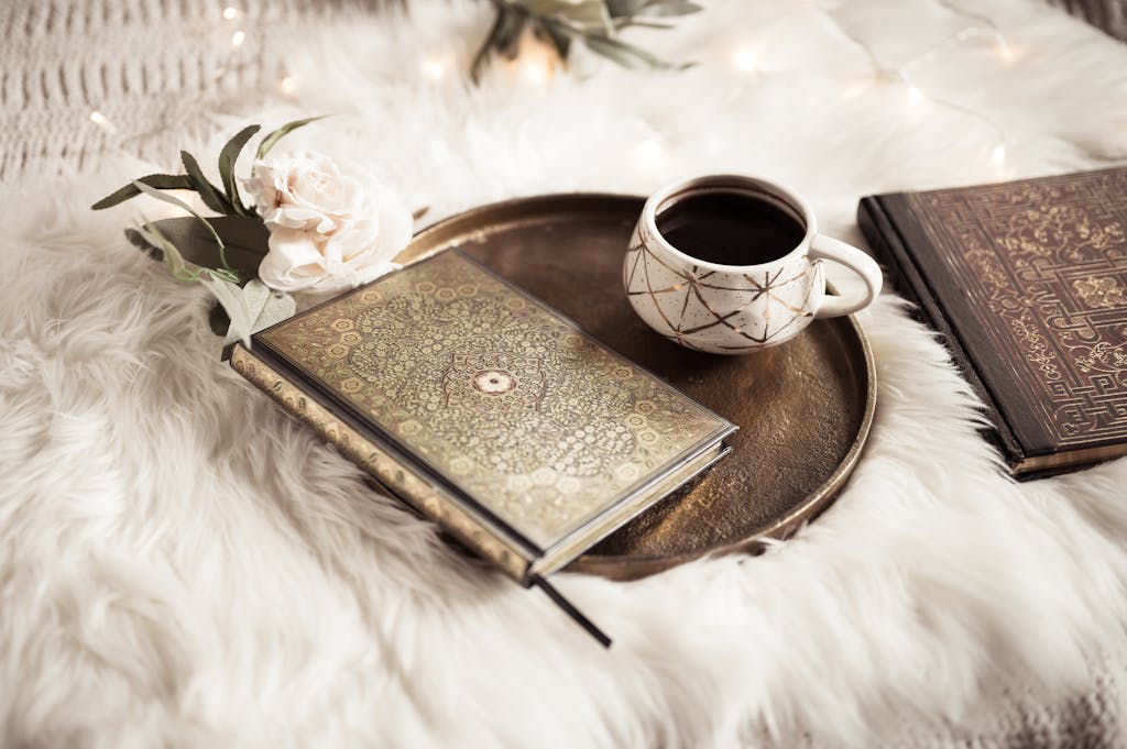 A cozy composition featuring ornate books and a coffee cup on a plush white fur background.