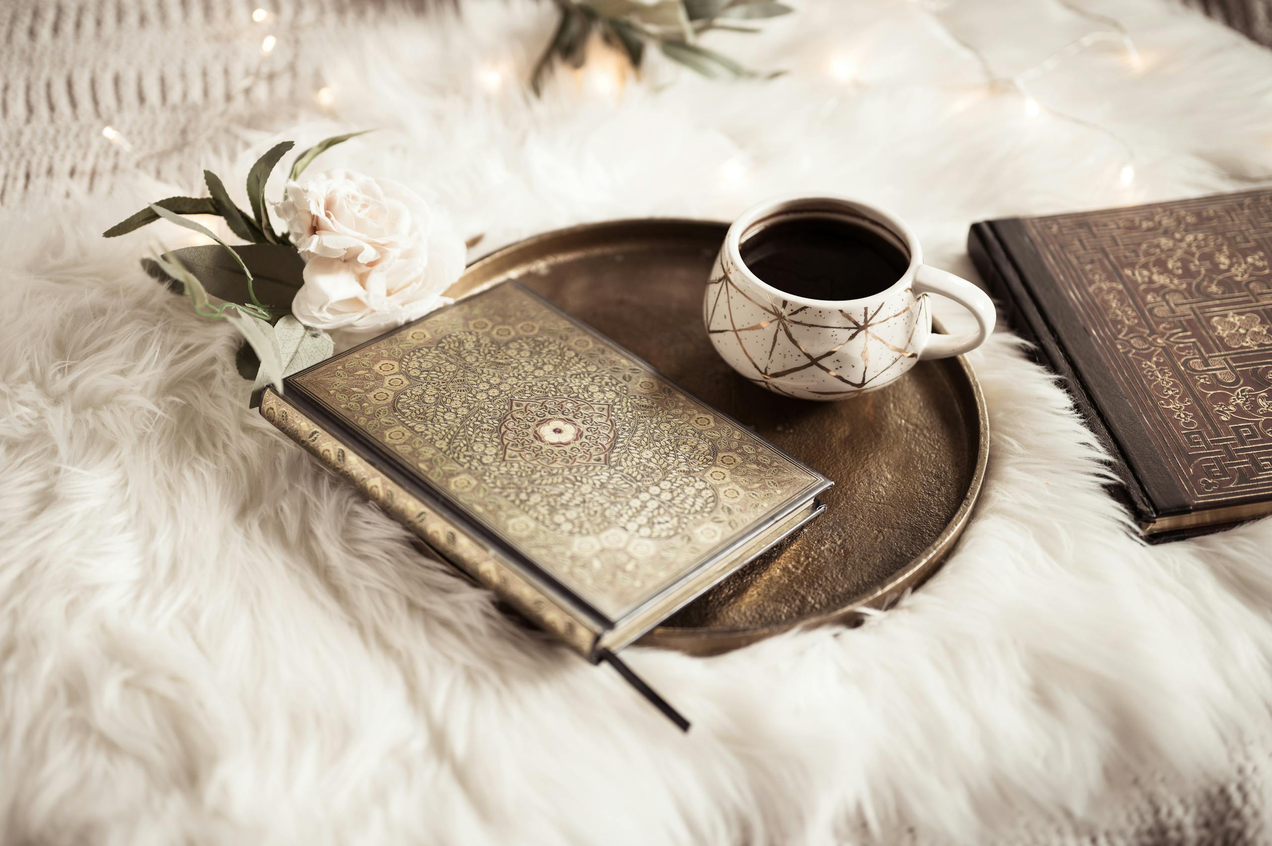 A cozy composition featuring ornate books and a coffee cup on a plush white fur background.