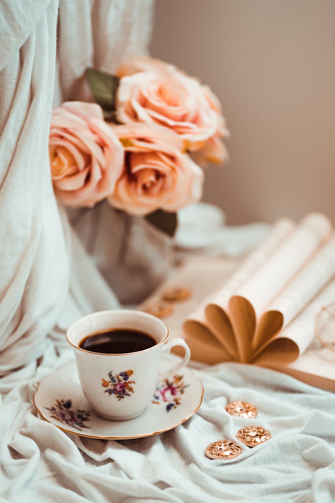 Charming setup with a floral teacup and saucer, roses, and golden pens on a soft fabric background.