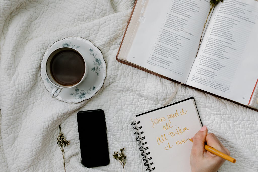 Flat lay of Bible study with coffee, notebook, and phone on a quilted blanket.